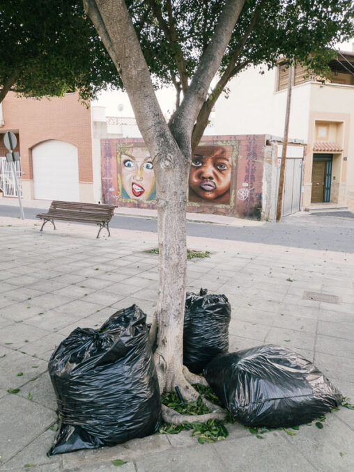 Bolsas de basura en una calle de Almería parecen ser observadas por los dos personajes de un graffiti.